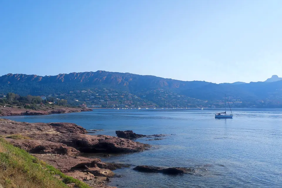 Falaises rouges et une baie bleue avec un bateau au mouillage