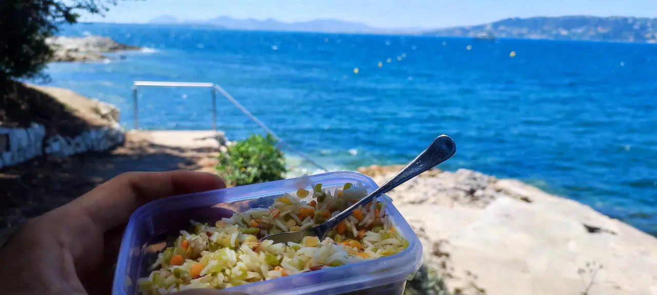 Plate of local food held above bright blue sea during a coastal ride