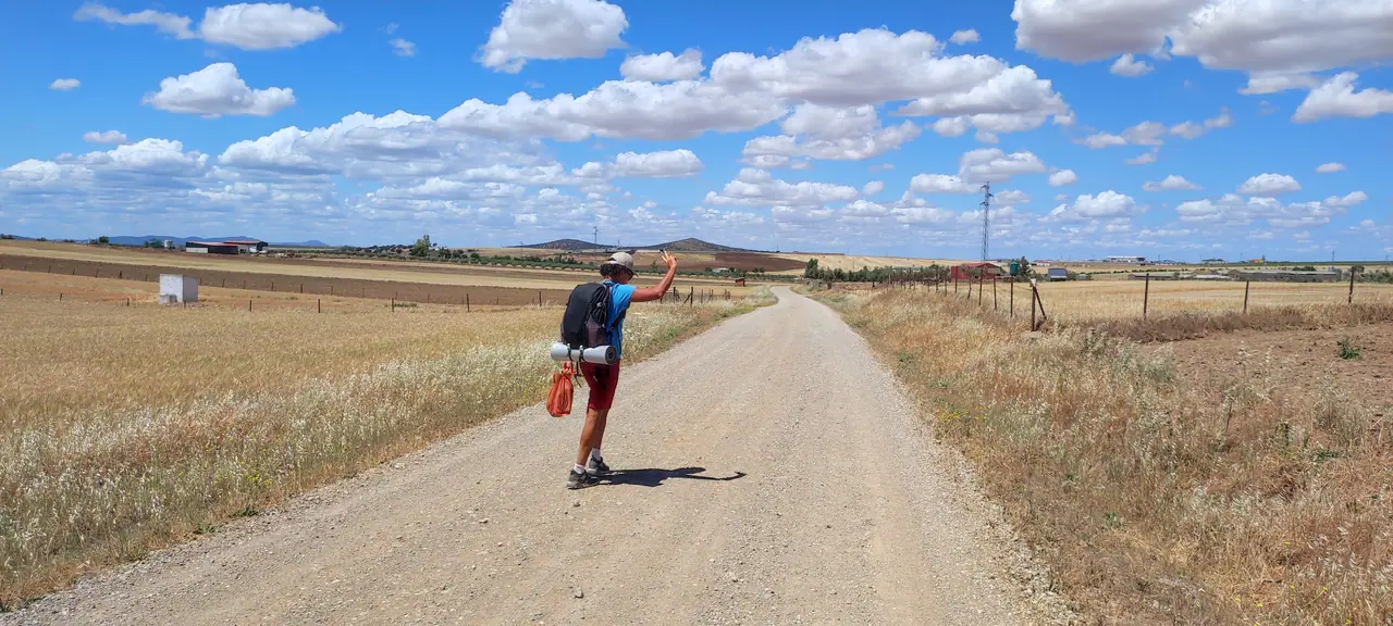 Cyclist on a straight white gravel road through flat open fields under blue skies