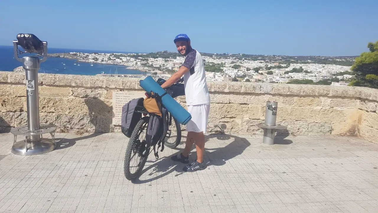 Cyclist with a loaded Trek bicycle at a stone viewpoint above the blue sea