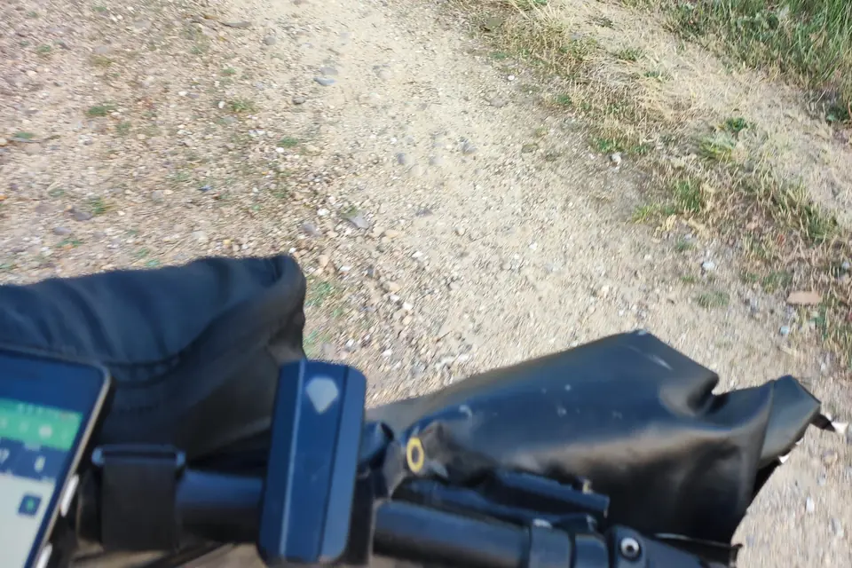 Handlebar with GPS unit and bags while riding a stony track