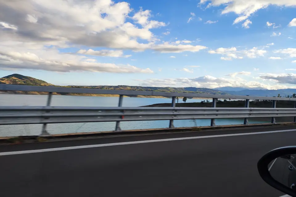 Coastal road with guardrail running beside a calm lagoon