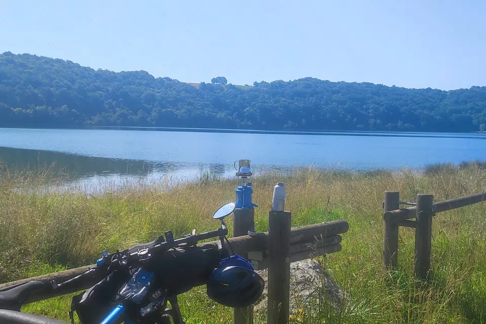 Handlebar with bar bag in front of a lake and a wooden fence