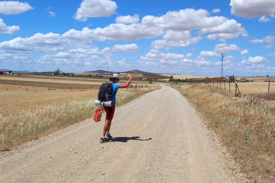 Cyclist walking beside the bike on a wide gravel road across open fields