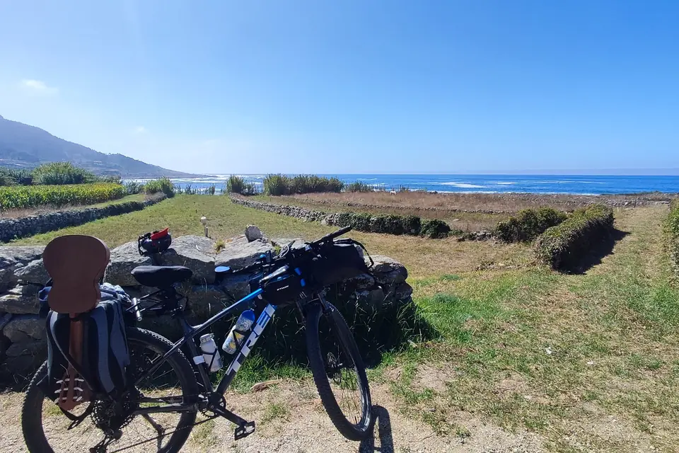 Bike parked on a grassy field with a low stone wall and the sea beyond