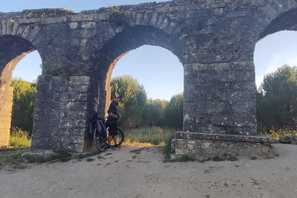 Loaded touring bike leaning under the arch of an old stone aqueduct