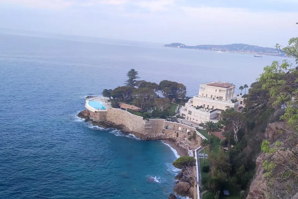 Coastline from above with a villa on a green promontory and a pool