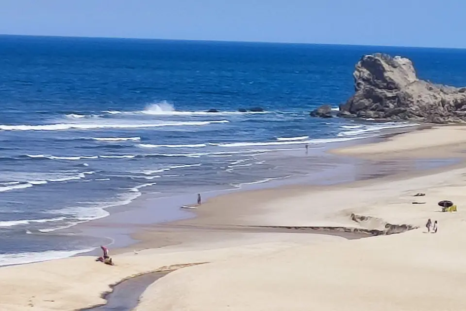 Sandy beach with breaking waves and a rock rising from the sea