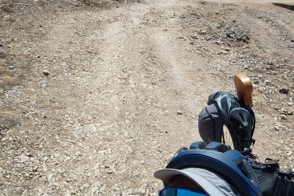 Loose gravel climb seen from the saddle, front bag in the frame