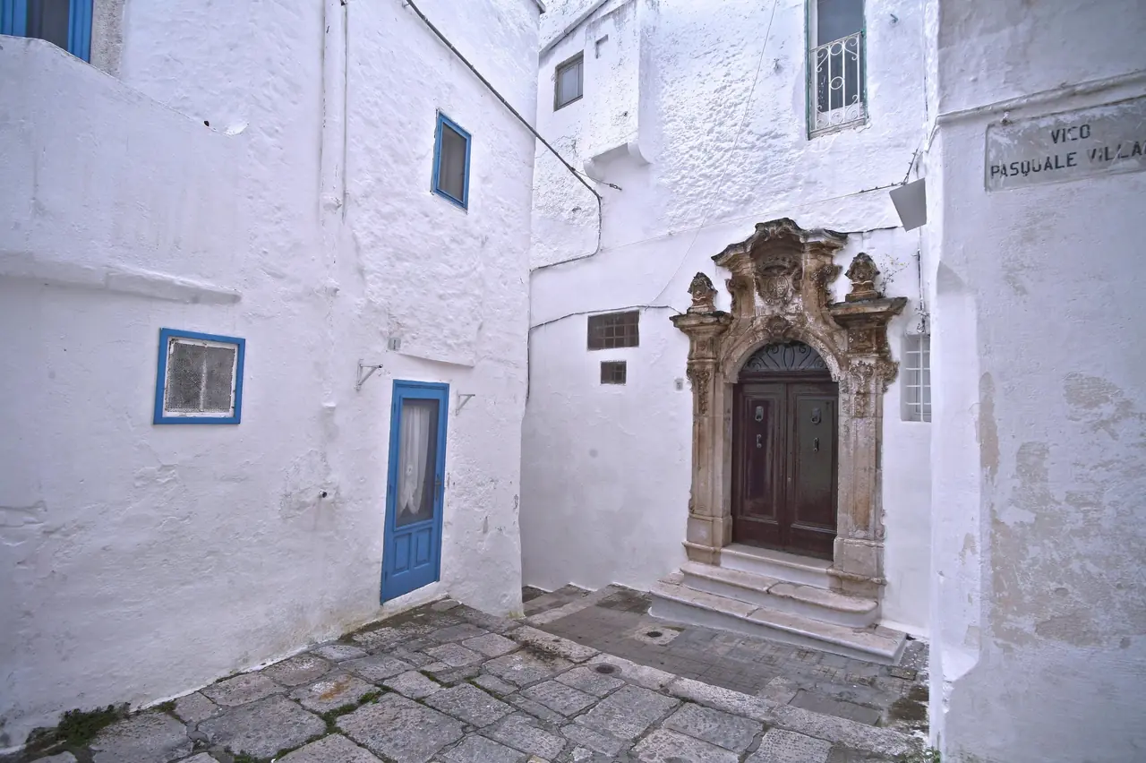 Narrow lime-washed white alley in the old town of Ostuni, with steps and flower pots along the walls