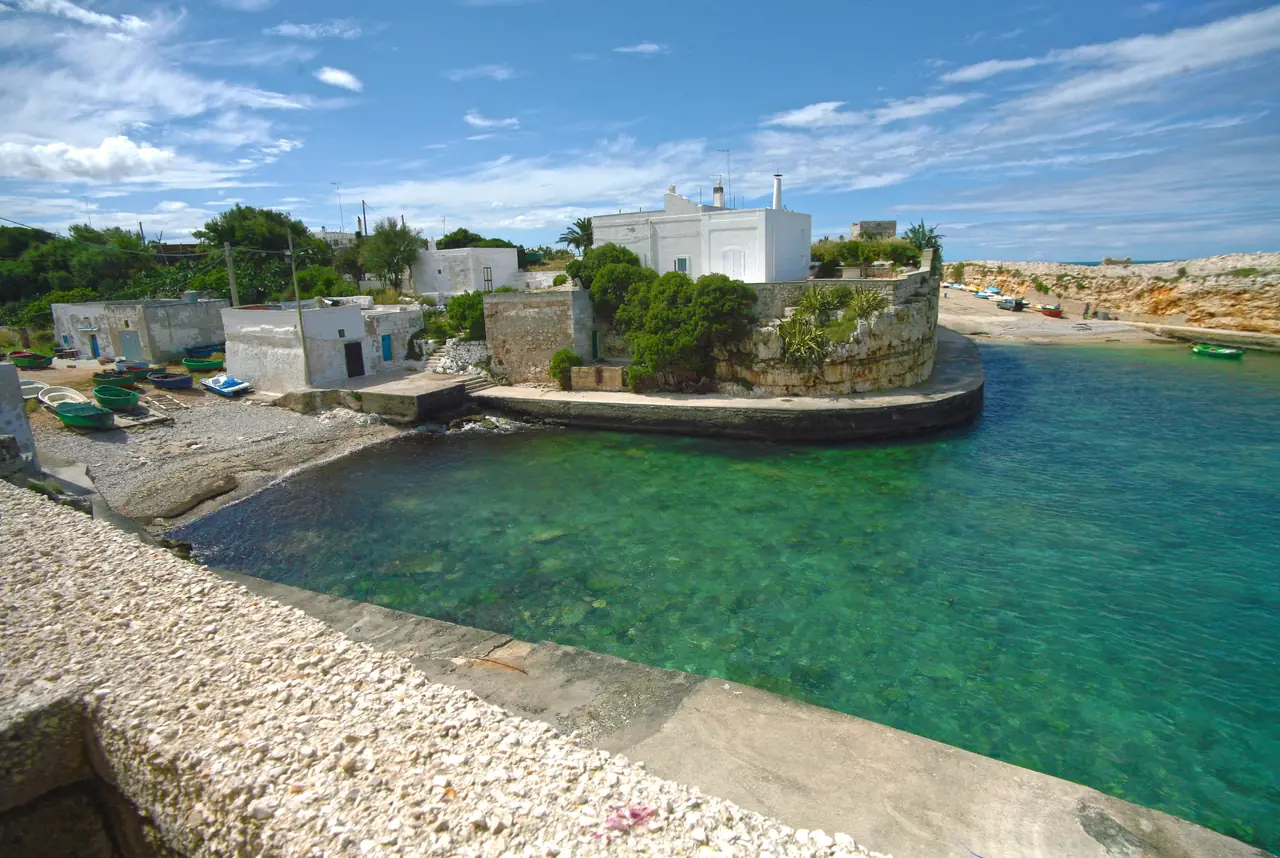 The bay of Cala Paura in Polignano a Mare with fishing boats moored and the low rocky shore behind